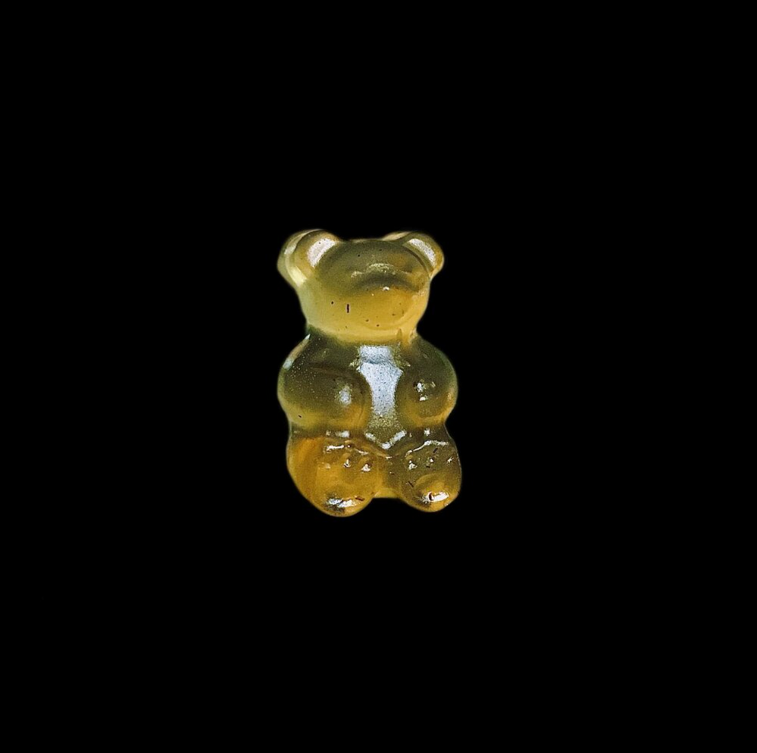 A yellow gummy bear with a black background.